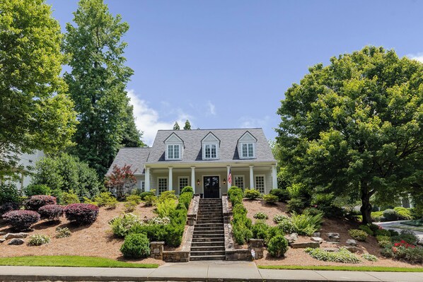 A two-story house with a front porch, steps leading up to the entrance, and a flag. - Luxury 5BR Buckhead Home | World Cup Ready (Atlanta)