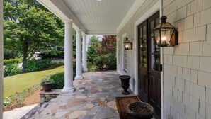 A covered porch with stone flooring, white columns, and a dark door. - Luxury 5BR Buckhead Home | World Cup Ready (Atlanta)