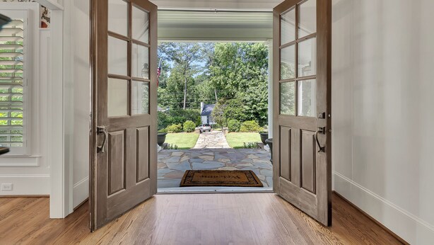A wooden door leading to a stone pathway with a doormat, surrounded by a white wall and a wooden floor. - Luxury 5BR Buckhead Home | World Cup Ready (Atlanta)