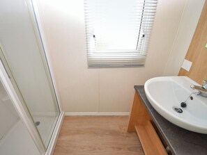 A bathroom with a glass shower door, a sink with a wooden vanity, and a window with blinds.