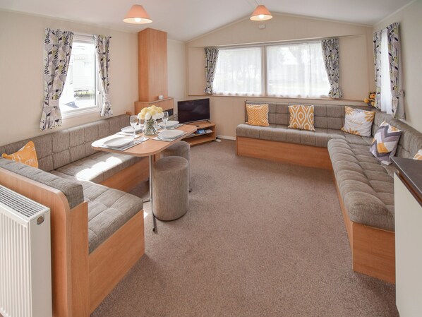 A modern living room with a sofa set, a dining table, and a TV.