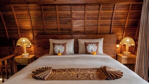 A neatly made bed with a decorative pillow arrangement and a branded bedspread in a wooden room with two bedside lamps. - Yama VIlla & SPA Ubud (Payangan)
