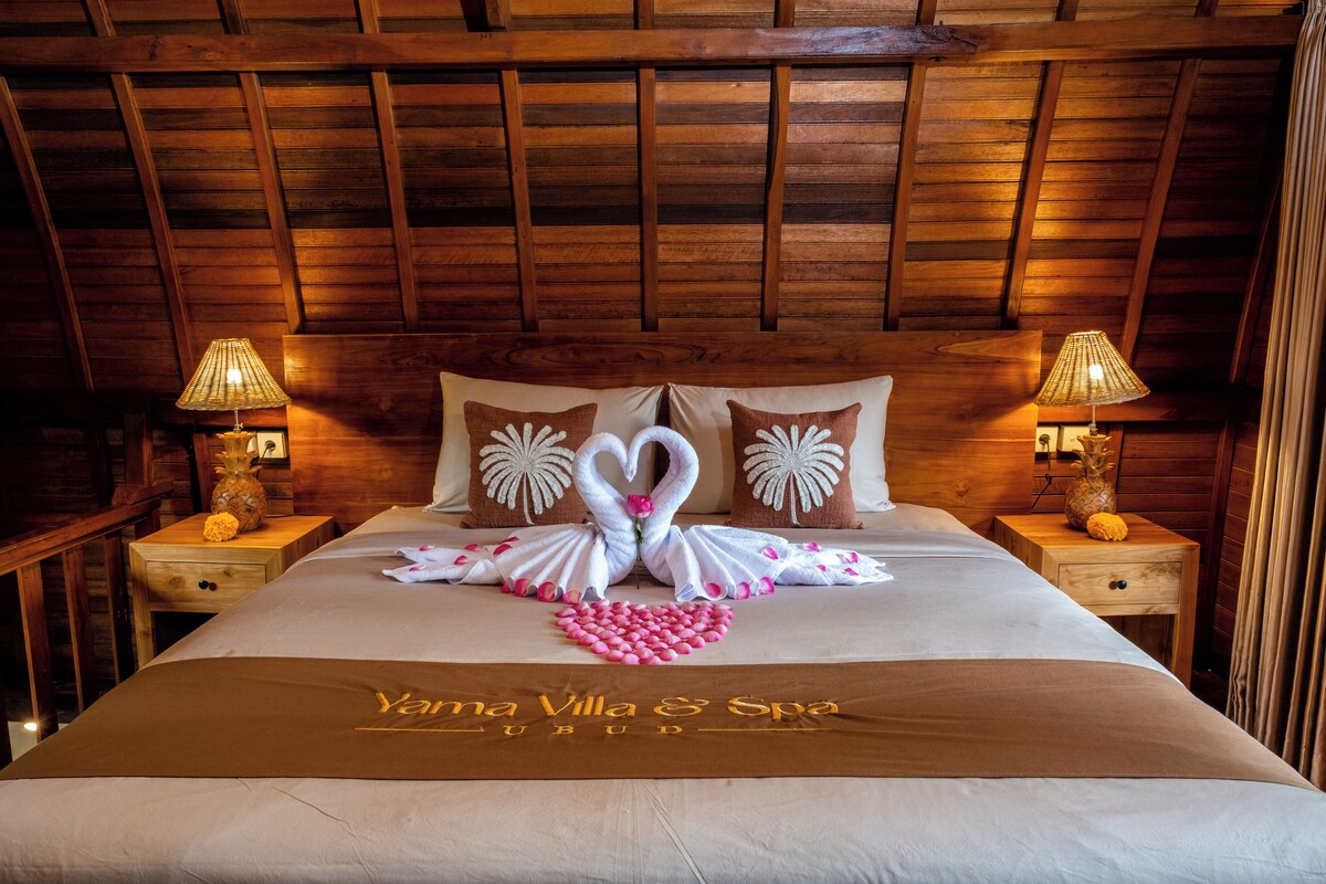 A neatly made bed with a swan towel decoration, wooden headboard, and two bedside lamps.