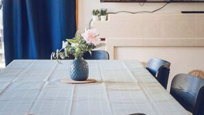 Un comedor con una mesa dispuesta para dos, un florero con flores y un cuadro de comida colgado en la pared.