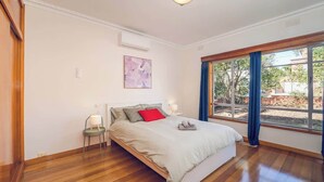 Un dormitorio con cama, mesita de noche, lámpara, ventana con cortinas y un cuadro en la pared.