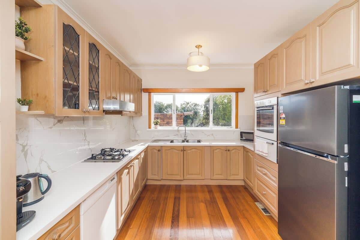 A kitchen with wooden cabinets, a stainless steel refrigerator, a gas stove, and a window with a view.
