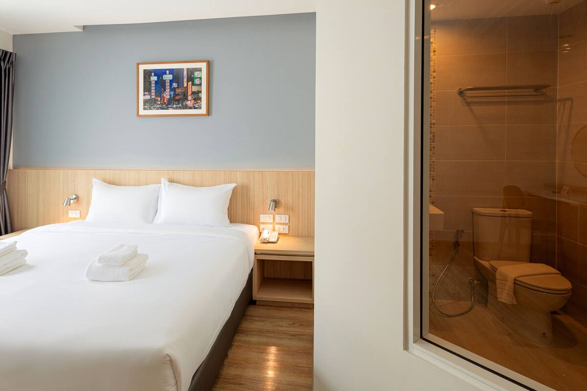 Une chambre d’hôtel avec un grand lit, une table de chevet avec une lampe, un tableau encadré au mur et une vue sur la salle de bain.