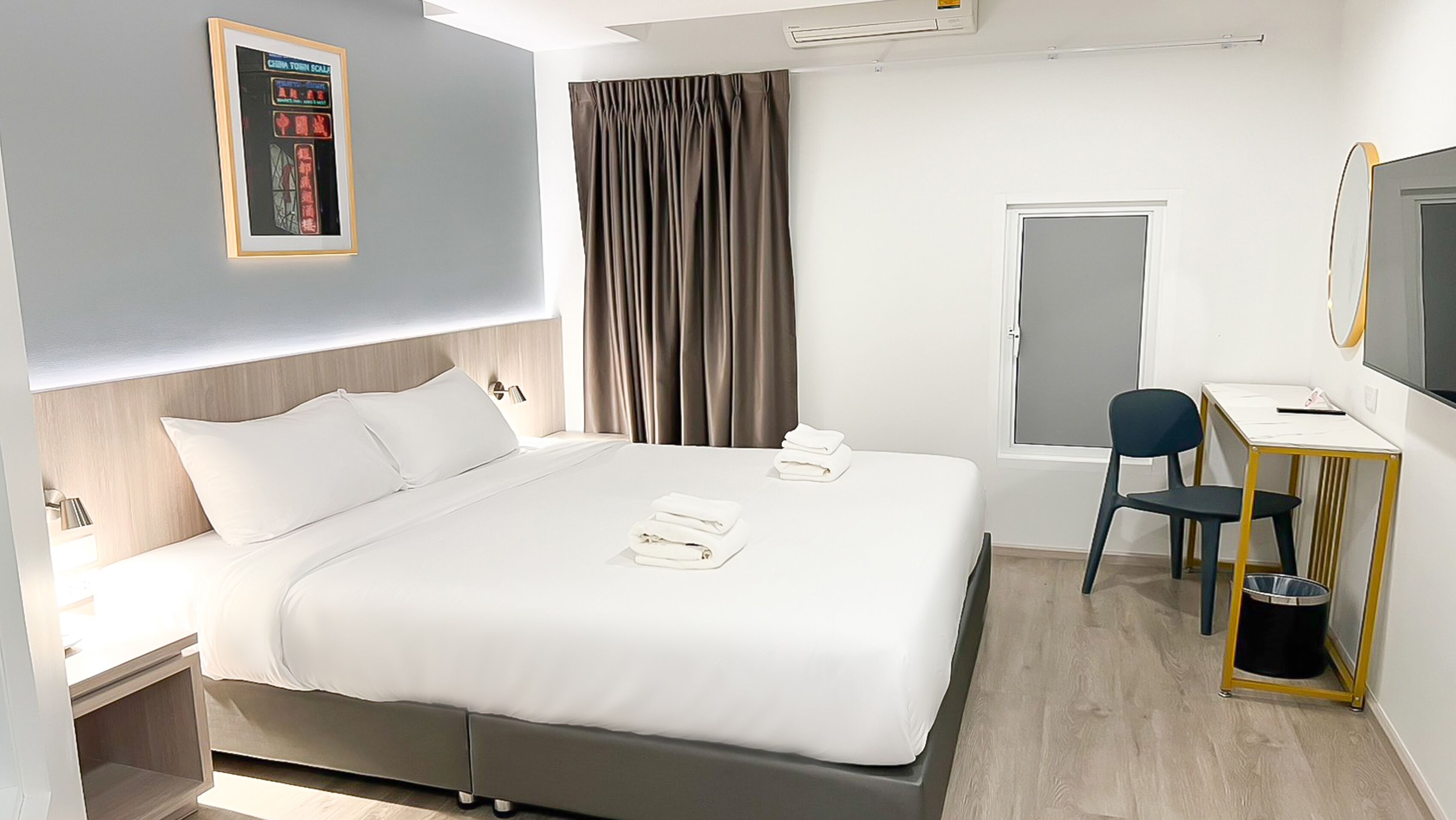 A modern hotel room with a large bed, a desk, a chair, a TV, and a window with curtains.