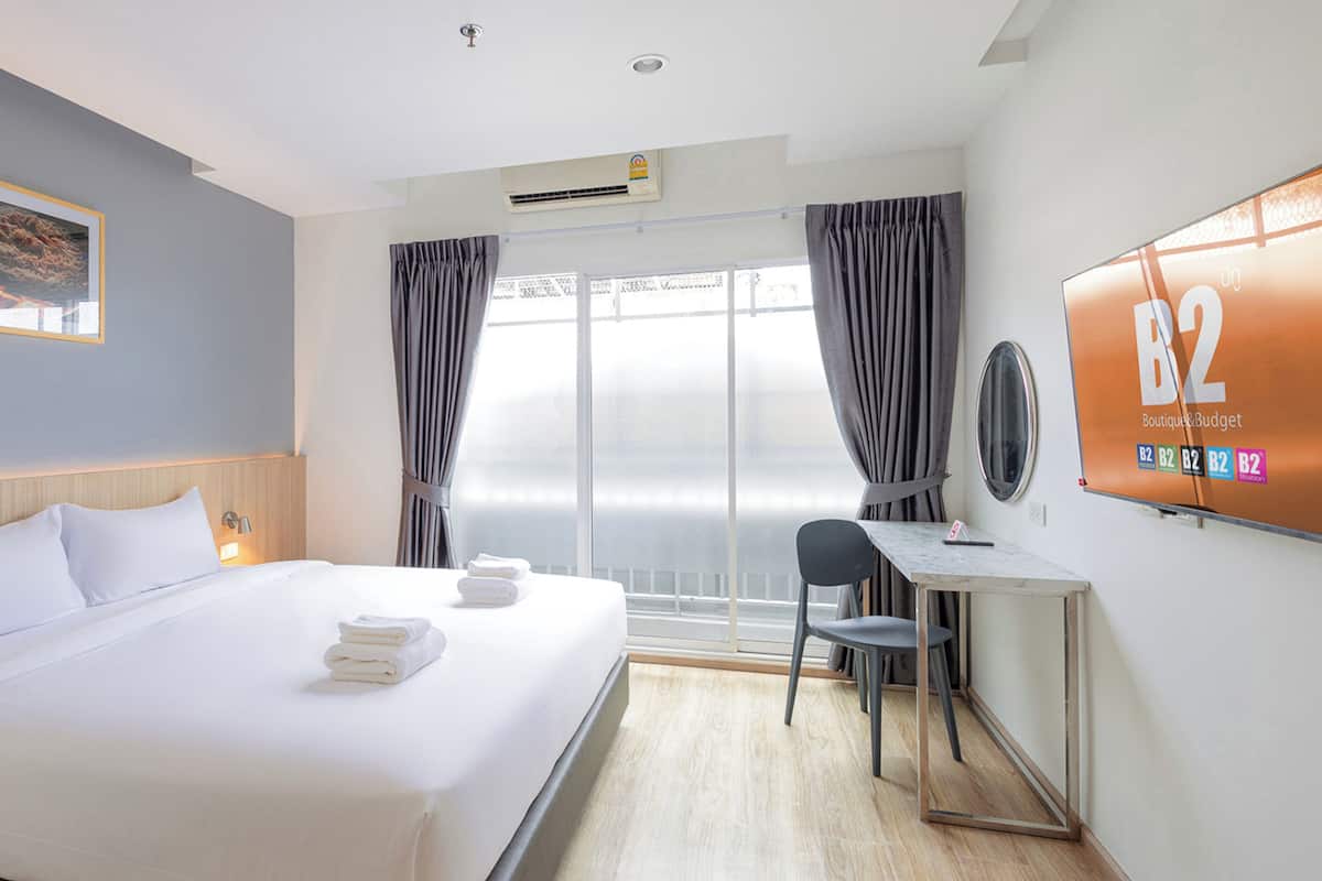 Une chambre d’hôtel avec un lit, un bureau, une chaise, une télévision et une fenêtre avec des rideaux.