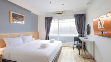 Une chambre d’hôtel avec un lit, un bureau, une chaise, une télévision et une fenêtre avec des rideaux.