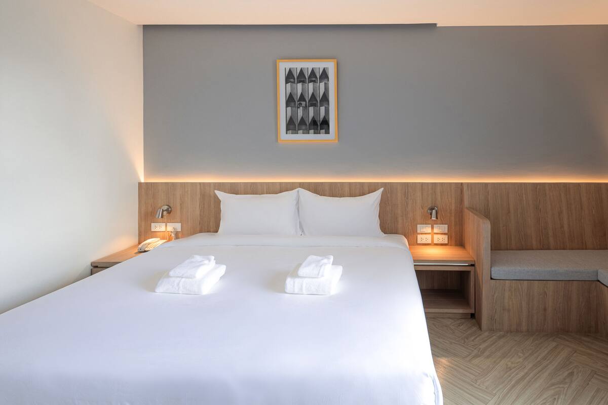 Une chambre d’hôtel moderne avec un grand lit, deux tables de chevet, un banc et un tableau encadré au mur.