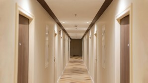 Een hotelgang met deuren aan beide kanten, een gestreept vloerkleed en inbouwverlichting.