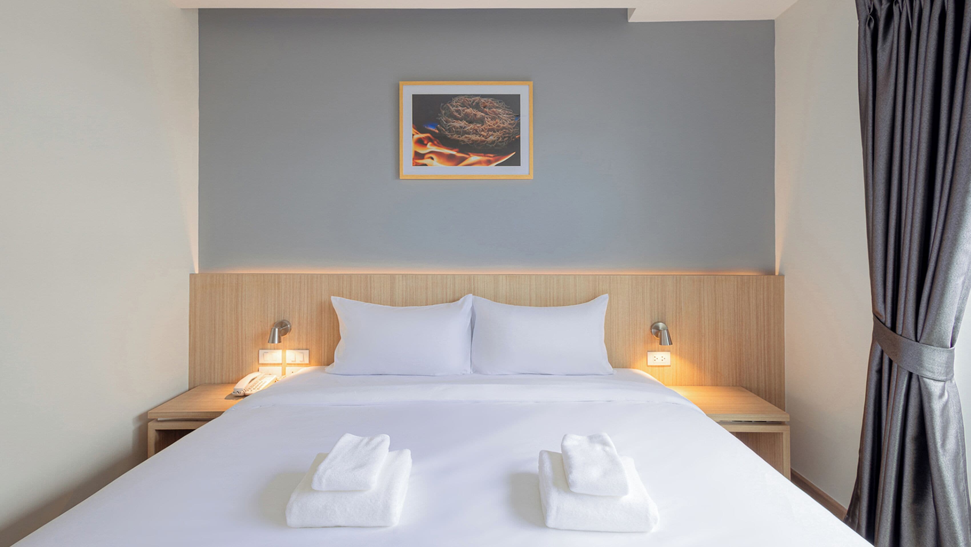 A hotel room with a neatly made bed, two bedside lamps, a wall-mounted picture, and a curtain.