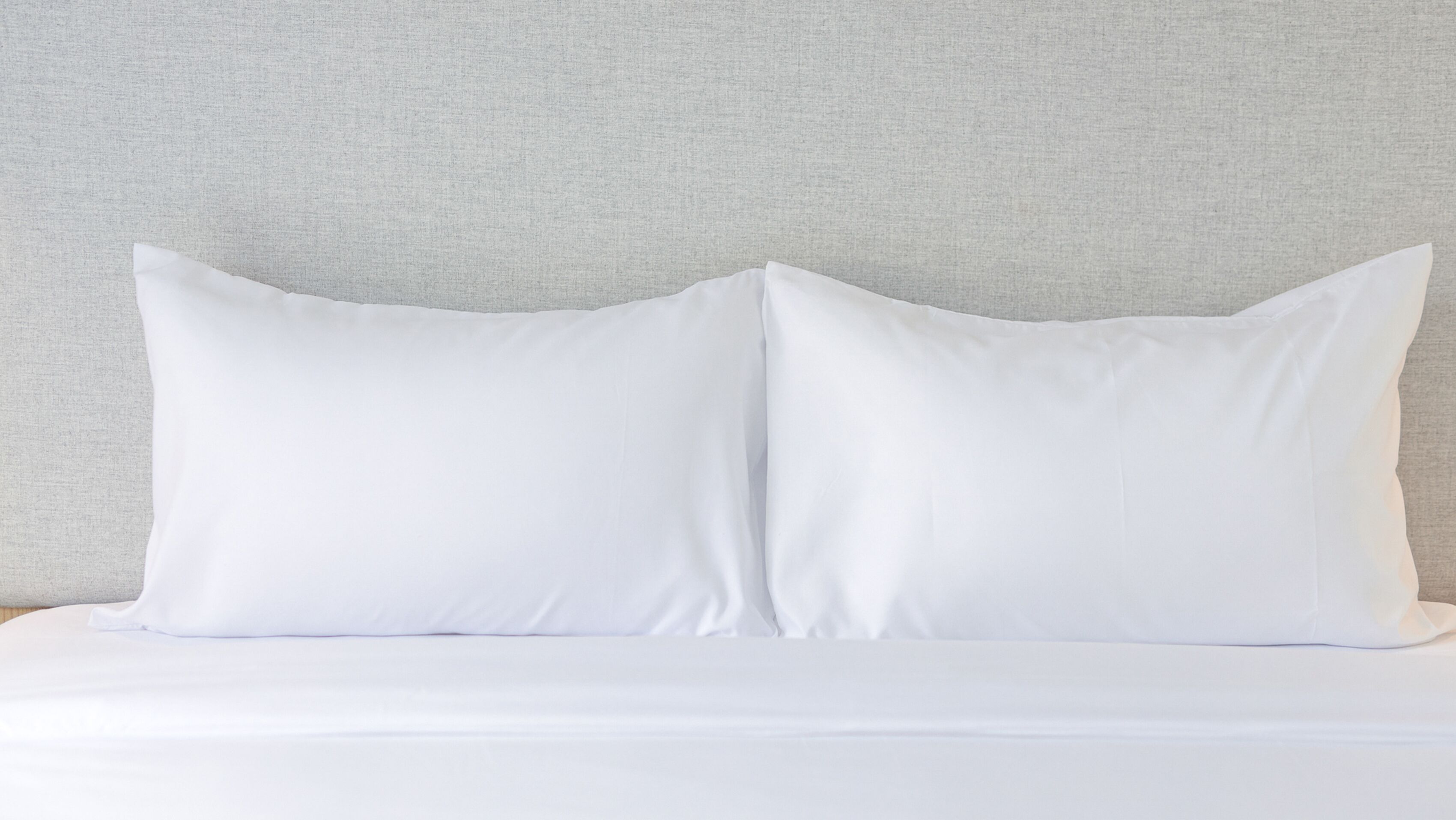 A bed with white bedding and two white pillows against a textured wall.