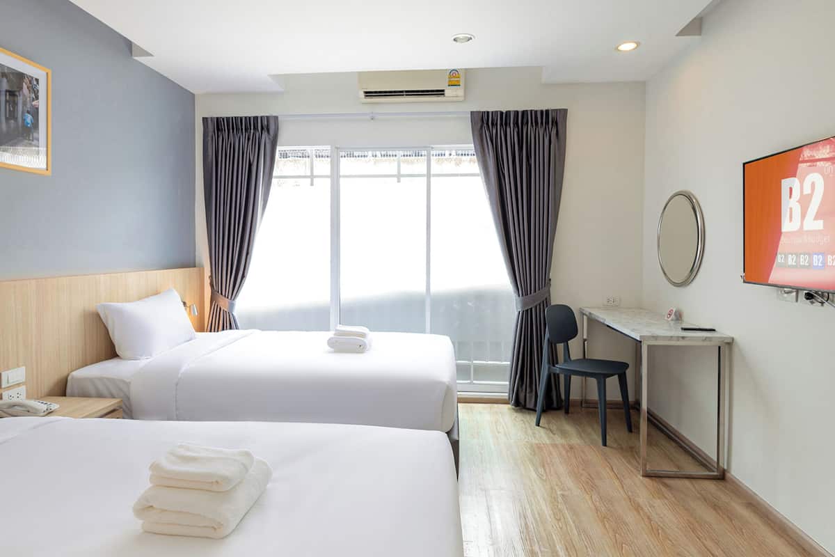 Une chambre d’hôtel avec deux lits, un bureau, une télévision et une fenêtre avec des rideaux.