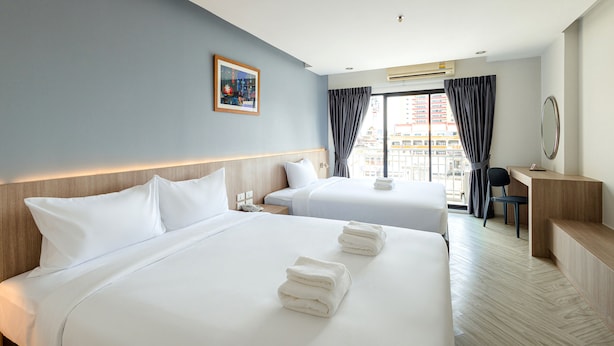 Een hotelkamer met twee bedden, een bureau, een stoel en een groot raam met gordijnen.