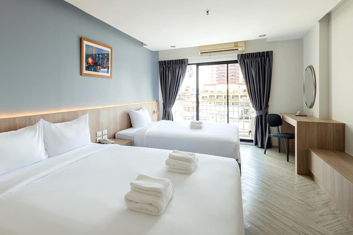 Une chambre d’hôtel avec deux lits, un bureau, une chaise et une grande fenêtre avec des rideaux.