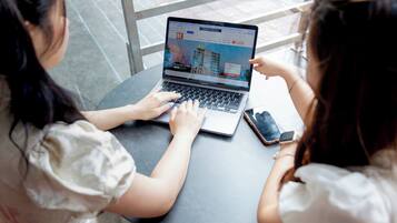 Two individuals using a laptop on a table with a smartphone nearby.