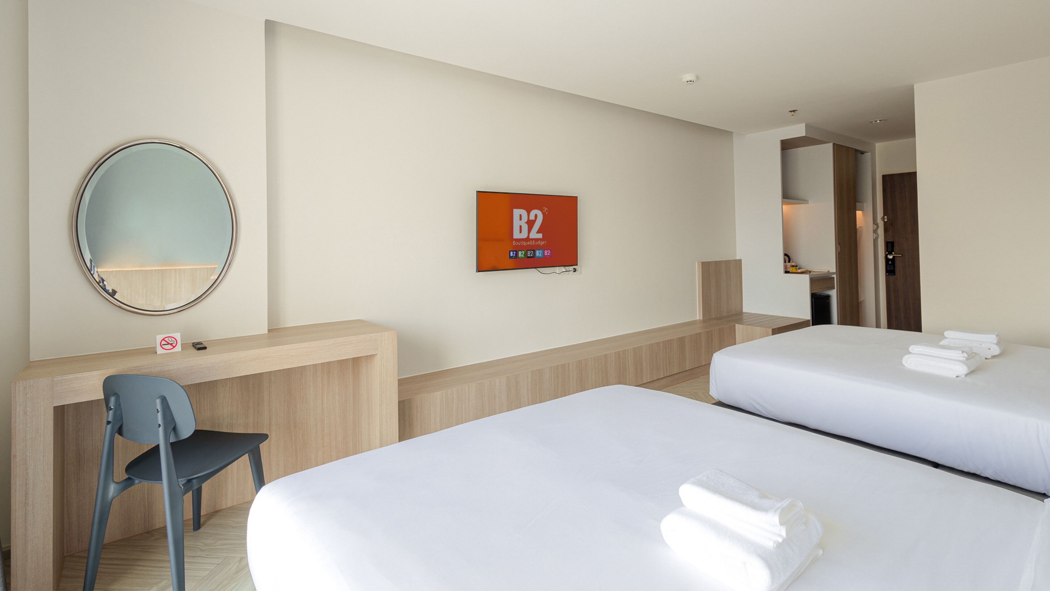 Habitación de hotel con dos camas, un escritorio, una silla, un espejo redondo y un cartel en la pared.