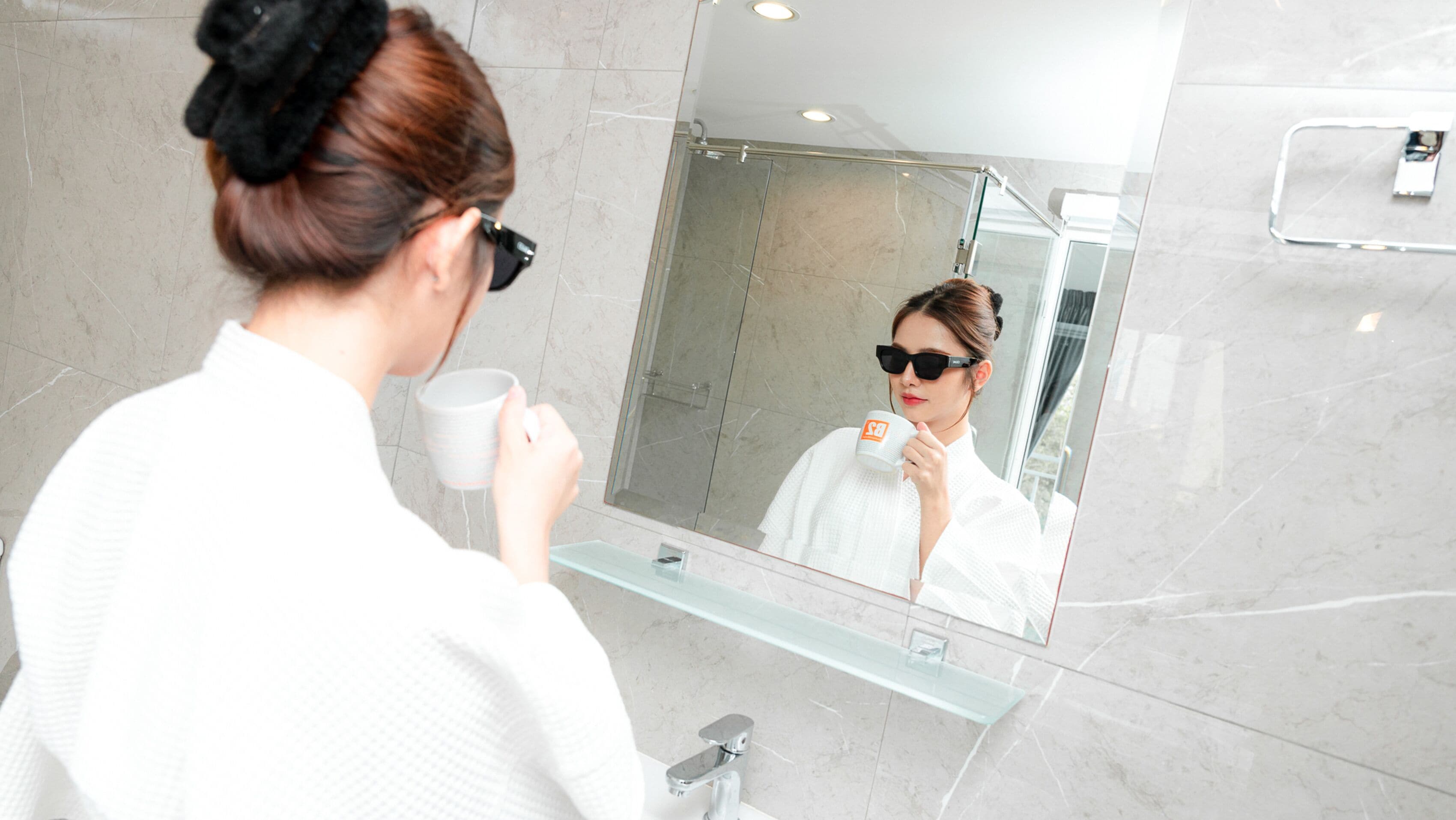A bathroom with a glass shower enclosure, a sink with a glass shelf, and a mirror reflecting the room.