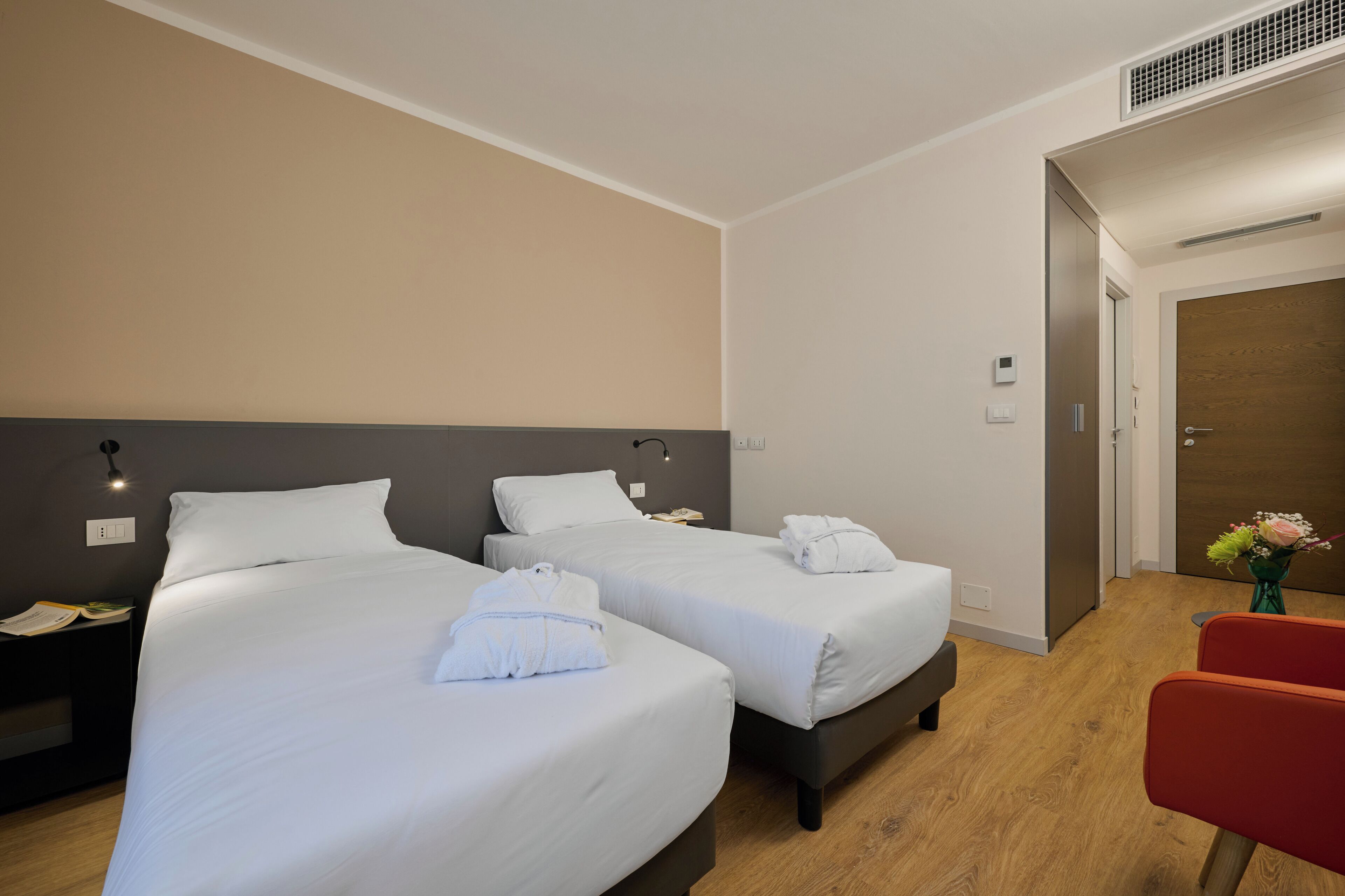 Une chambre d’hôtel avec deux lits, une chaise rouge et un plancher en bois.