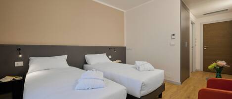 A hotel room with two beds, a red chair, and a wooden floor.