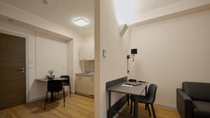 A modern, well-lit room with a wooden floor, a dining table with chairs, a black sofa, and a kitchenette in the background. - Zenit Park Hotel (Rivalta di Torino)