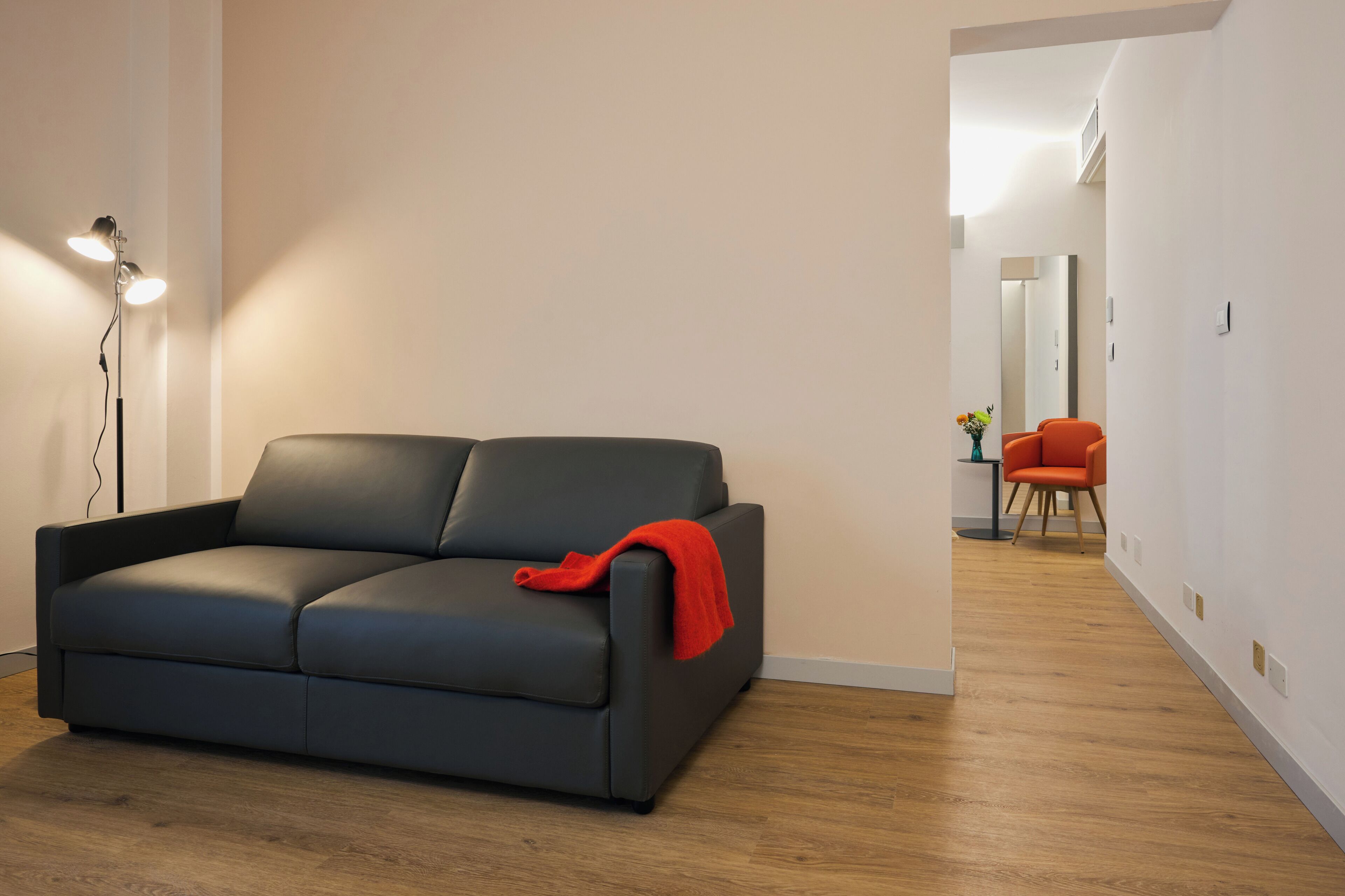 A modern living room with a dark grey sofa, a red throw blanket, and a floor lamp.