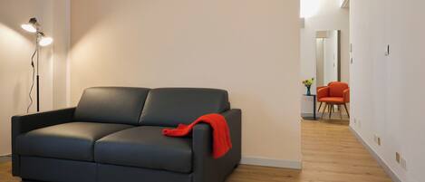 A modern living room with a dark grey sofa, a red throw blanket, and a floor lamp.
