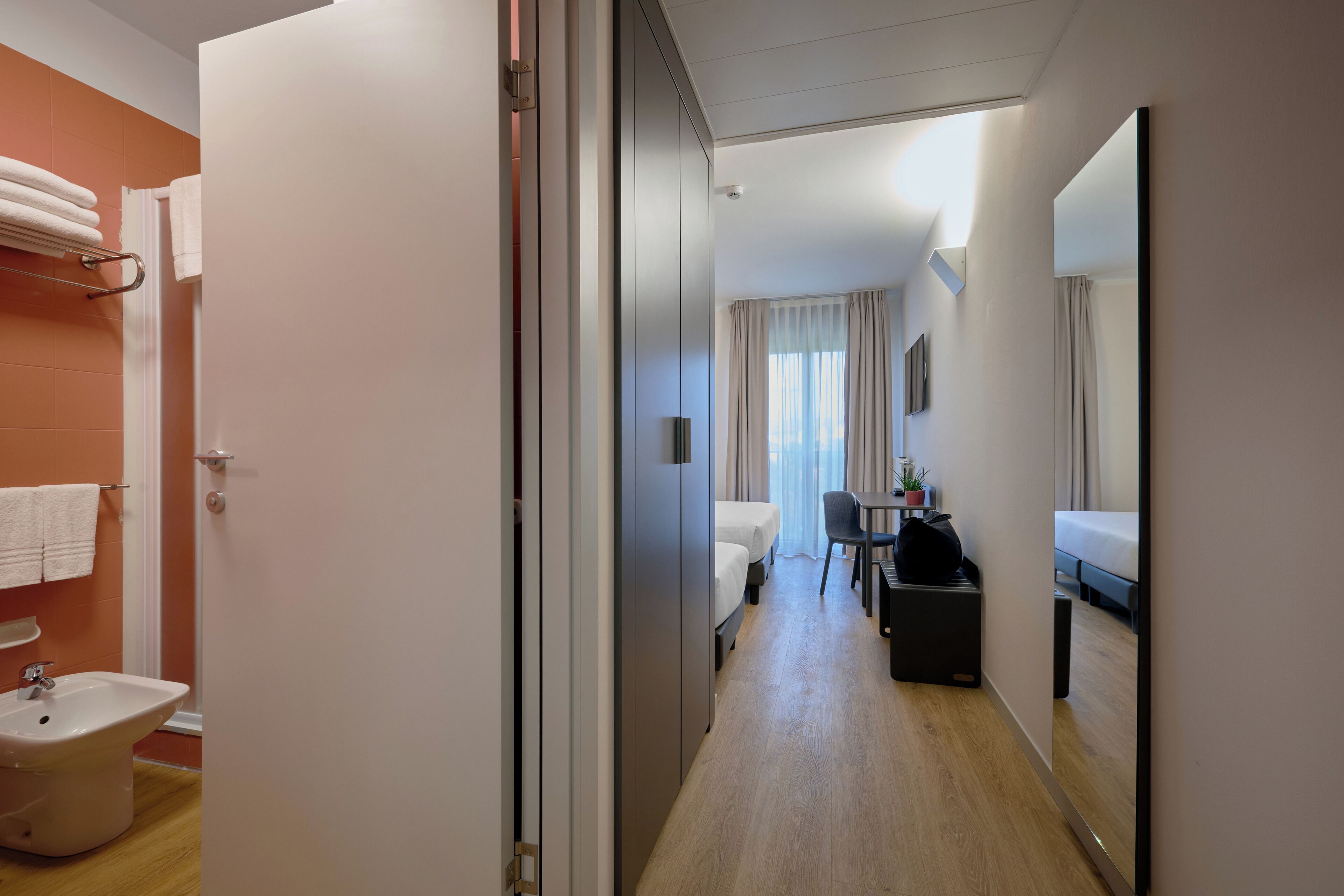 A hotel room with a bathroom, a bed, a desk, and a chair.