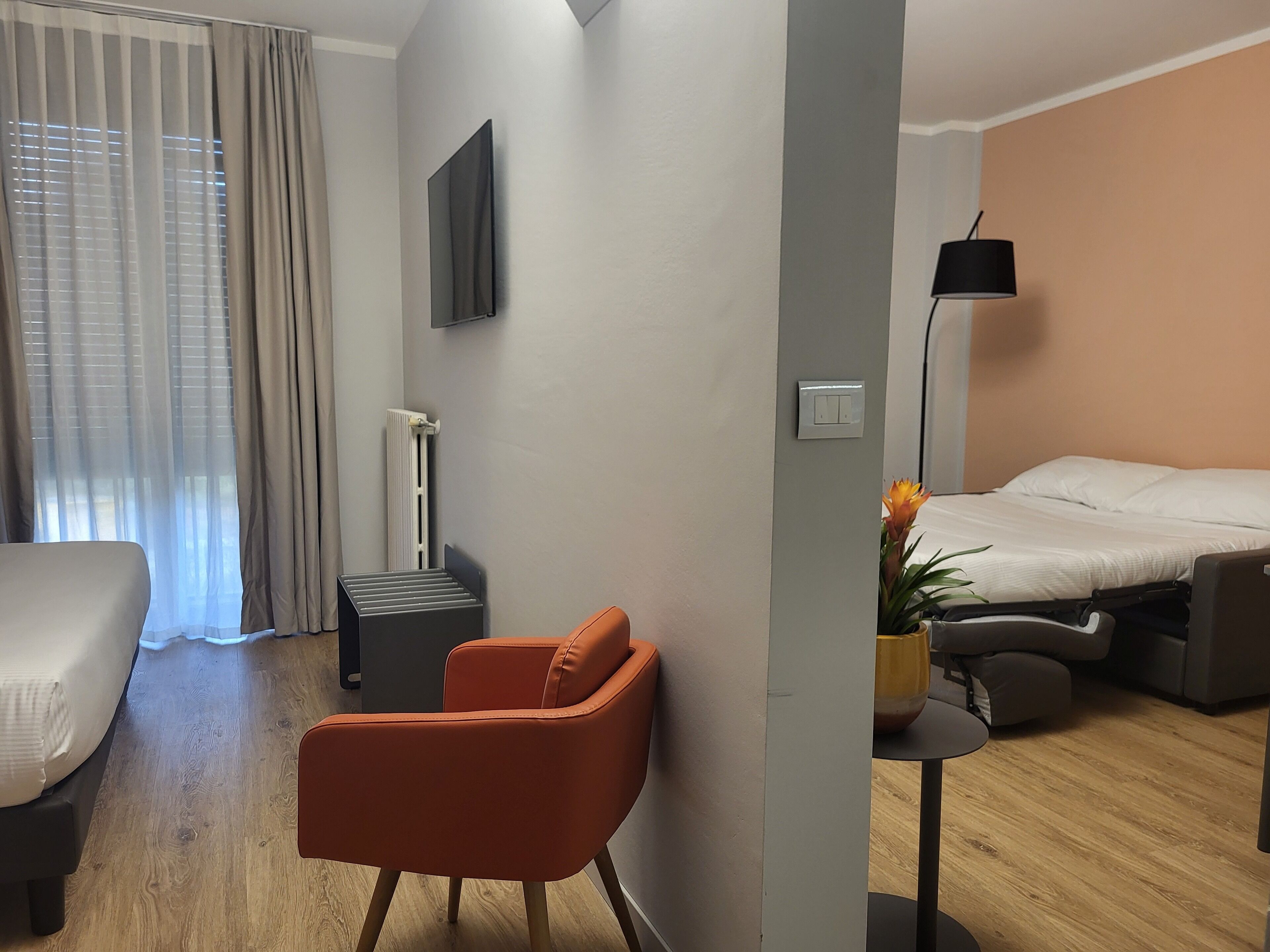 Una habitación de hotel con cama, escritorio, silla, televisión y ventana con cortinas.