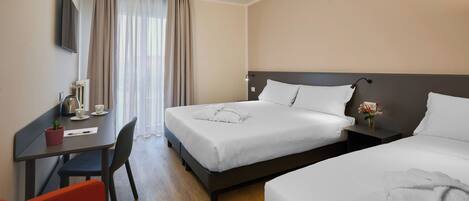 A hotel room with two beds, a desk with a chair, a TV mounted on the wall, and a window with curtains.