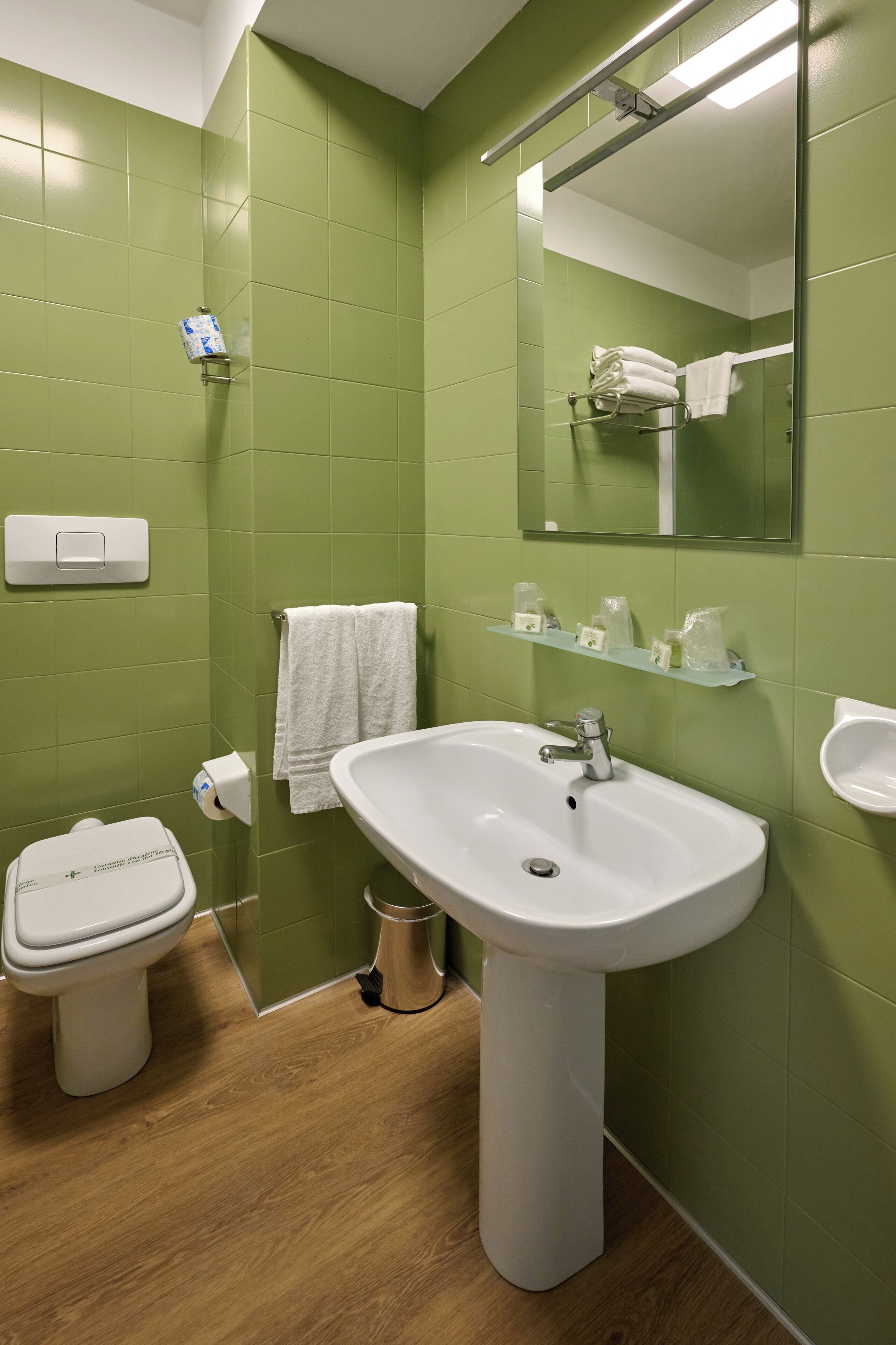 A bathroom with green walls, a white sink, a toilet, a mirror, and a towel rack.