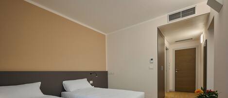 Quarto de hotel com duas camas, uma mesinha com um vaso de flores e uma porta que dá para outro quarto.