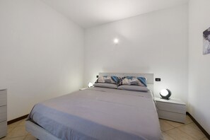 A bedroom with a bed, nightstands, a wall-mounted light, and a small artwork.