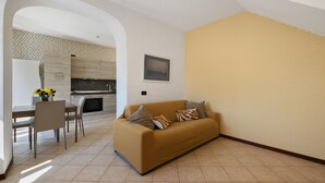 A living room with a sofa, a dining table with chairs, and a kitchen in the background.
