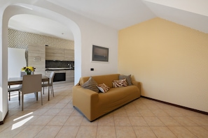 A living room with a sofa, a dining table with chairs, and a kitchen in the background.