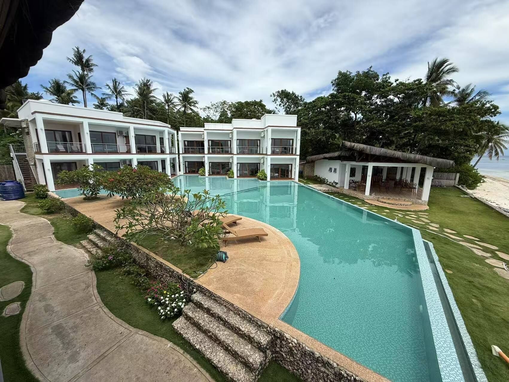 A modern resort with a large swimming pool, multiple guest rooms, and a beach view.