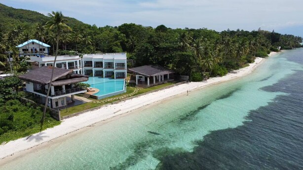 A beachfront property with a swimming pool, multiple buildings, and lush greenery.