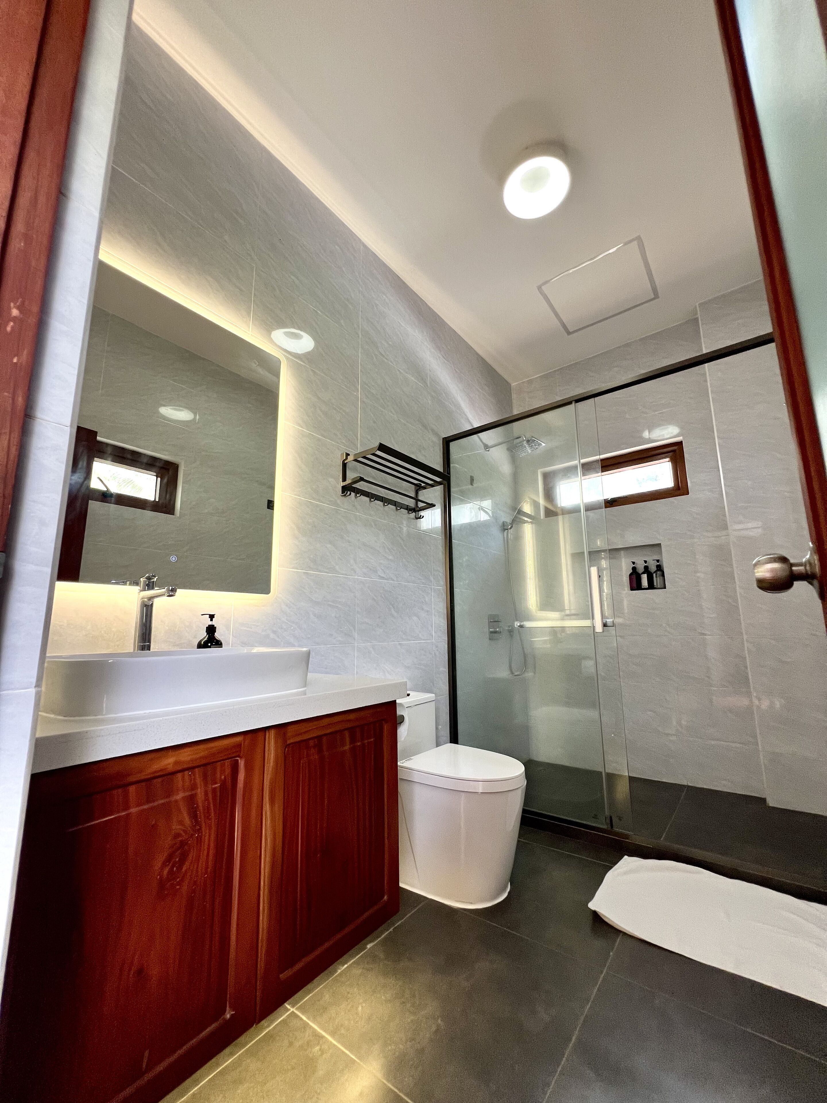 Une salle de bain moderne avec un grand miroir, un meuble-lavabo en bois, des toilettes blanches et une cabine de douche en verre.
