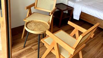 A room with a bed, two wooden chairs with woven seats, a small wooden table, and a wall-mounted light fixture.