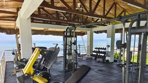 A gym with weightlifting equipment and a bench, overlooking a beach.