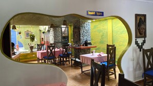 A restaurant with a stone wall, wooden chairs, and tables covered with pink tablecloths. - parachichi house Bed and Breakfast  (Arusha)