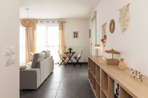 Una sala de estar con un sofá, una mesa de centro y un televisor. Hay una ventana con cortinas, una lámpara de pared y una planta pequeña sobre la mesa.