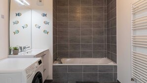Een moderne badkamer met een ingebouwde wasmachine, een badkuip en een grote spiegel met visstickers.