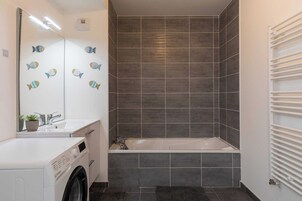Un baño moderno con lavadora incorporada, bañera y un espejo grande decorado con motivos de peces.