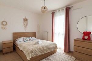 Un dormitorio con cama de madera, mesitas de noche, un espejo, un oso de peluche rojo y adornos decorativos en la pared.