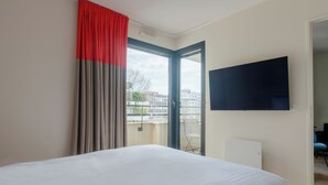 Et hotelværelse med en stor seng, et fjernsyn monteret på væggen og en balkon med udsigt til bygninger.