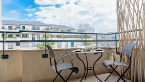 En balkon med to stole og et lille bord, med udsigt over et boligområde med flere bygninger.