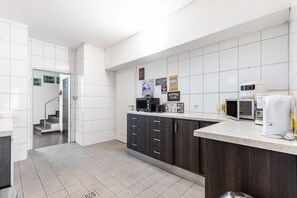 A modern kitchen with white tiles, dark wooden cabinets, a microwave, a coffee maker, and a refrigerator.